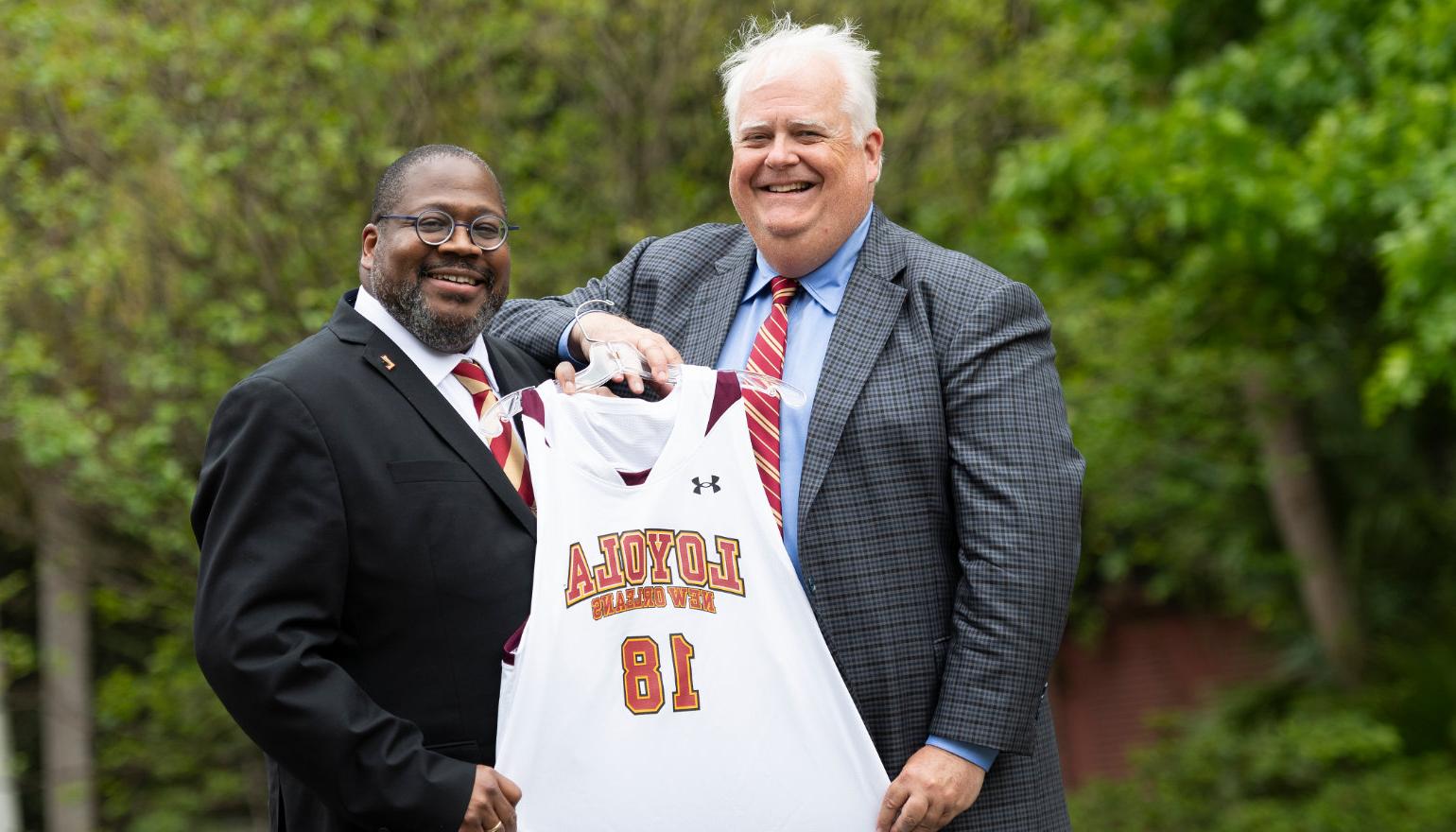 Stephen L和ry '83, chair of the Board of Trustees, presents Dr. Xavier 科尔 with a #18 basketball jersey